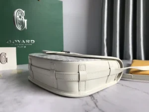 Goyard Belv é d è re Single Mailman Bag in white leather, showcasing a minimalist design with adjustable shoulder strap, set against a green Goyard box and elegant backdrop.