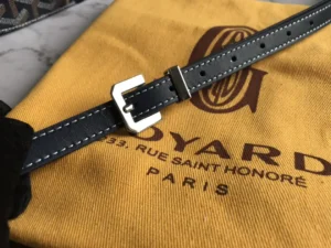 Goyard bag strap with sleek buckle on yellow fabric featuring Goyard logo and Paris address, highlighting luxury craftsmanship and minimalist design.