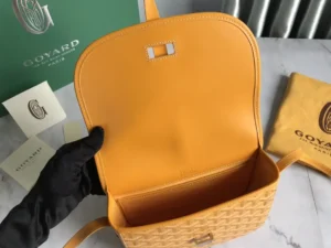 Interior view of Goyard Belv é d è re Single Mailman Bag showcasing yellow lining, metal clasp, and woven exterior, with brand packaging visible.
