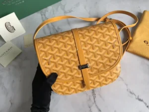 Goyard Belv é d è re Single Mailman Bag in yellow, featuring a narrow buckle, adjustable shoulder strap, and textured fabric, presented on a marble surface with branded packaging.