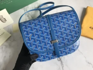 Goyard Belv é d è re Single Mailman Bag in blue with a signature pattern, featuring a narrow buckle and adjustable shoulder strap, displayed on a marble surface alongside branded packaging.