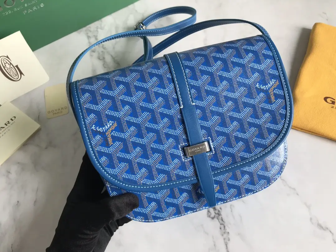 Goyard Belv é d è re Single Mailman Bag in blue with signature pattern, featuring adjustable shoulder strap and leather accents, displayed on marble surface with Goyard branding.