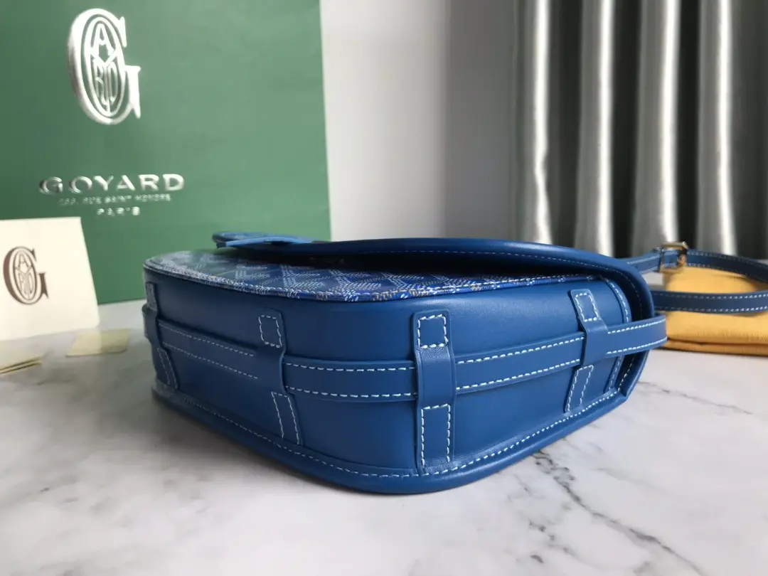 Goyard Belv é d è re Single Mailman Bag in blue leather with a patterned top, showcasing adjustable shoulder strap and elegant design against a green backdrop.