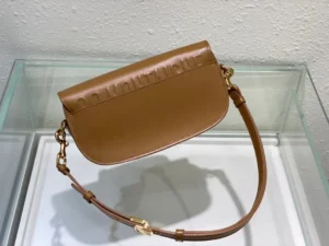 Dior Bobby East-West Bag in tan leather, showcasing a sleek crescent shape and detachable shoulder strap, displayed in a minimalist setting.
