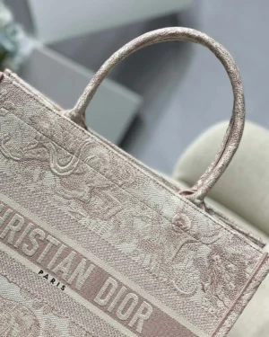 Dior Book Tote Bag in pink with intricate floral pattern and "CHRISTIAN DIOR PARIS" logo, showcasing luxury design and craftsmanship.