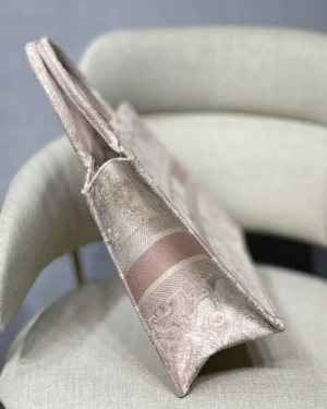 Dior Book Tote Bag in elegant pink fabric, showcasing intricate patterns and spacious design, placed on a light-colored chair, emphasizing luxury and style.