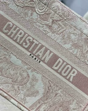 Christian Dior logo on the Dior Book Tote Bag, featuring intricate detailing and a soft pink color palette, emphasizing luxury and style.