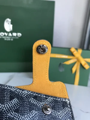 Close-up of Goyard MontMartre GM bag strap with yellow leather detail against a green Goyard box and ribbon, highlighting luxury craftsmanship and brand identity.