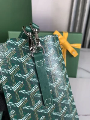 Goyard MontMartre GM Green bag featuring a distinctive green pattern, zipper closure, and leather strap, alongside a gift box with a yellow ribbon, highlighting its stylish and functional design.