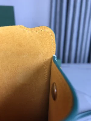 Interior view of Goyard MontMartre GM Green wallet showcasing yellow lining and embossed logo detail, emphasizing luxury craftsmanship and stylish design.