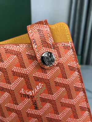 Close-up of Goyard MontMartre GM bag in orange, showcasing signature pattern, logo button, and contrasting yellow interior.