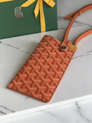Goyard MontMartre GM bag in orange with signature pattern, displayed on marble surface alongside a green Goyard gift box, emphasizing stylish accessory for men and women.