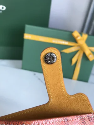 Close-up of Goyard MontMartre GM bag's interior with yellow leather strap and metal snap button, featuring green gift box in background.