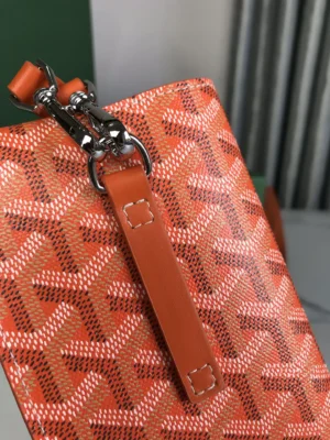 Close-up of Goyard MontMartre GM bag in orange, showcasing distinctive pattern, zipper detail, and strap, emphasizing stylish accessory for street fashion.