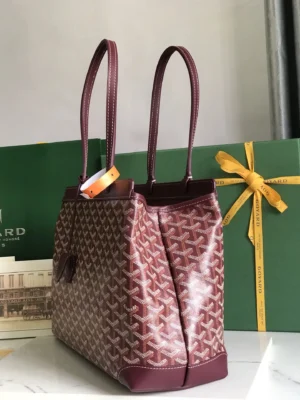Goyard Tote Bag Commuter Series in burgundy with dual handles and signature pattern, displayed next to a green Goyard gift box with a yellow ribbon.