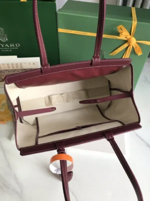 Interior view of a Goyard Tote Bag Commuter Series in burgundy, showcasing spacious compartments and a protective canvas lining, with branded green packaging in the background.