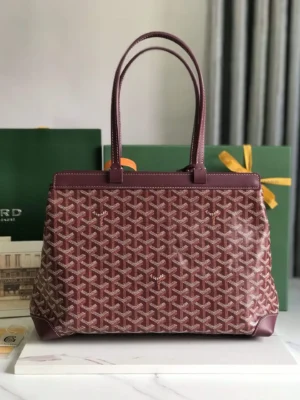 Goyard Tote Bag Commuter Series in burgundy with a spacious interior, stylish design, and two flat handles, displayed against a green backdrop.