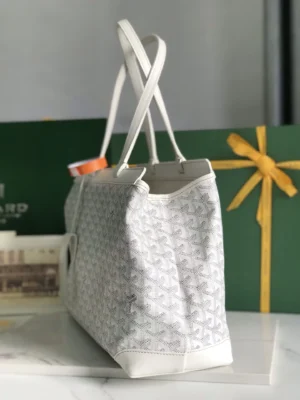 Goyard Tote Bag Commuter Series in white canvas with signature pattern, featuring flat handles and spacious design for commuting, displayed against a green background with a gift ribbon.