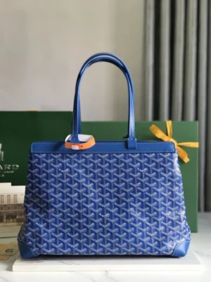 Goyard Tote Bag Commuter Series in blue with distinctive pattern, featuring two handles and a protective cover, set against a green backdrop with a gift ribbon.