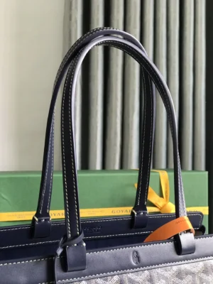 Goyard Tote Bag Commuter Series with navy leather handles, showcasing stitching details and a protective cover, against a green Goyard box and curtains in the background.