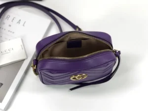 Purple Gucci GG Marmont small shoulder bag with interlocking Double G logo, unzipped to showcase interior, placed on a white surface with magazine and brand logo visible.
