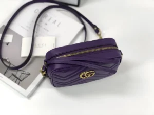 Purple Gucci GG Marmont small shoulder bag with interlocking double G logo, placed on a white surface with magazines.