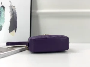 Purple Gucci GG Marmont small shoulder bag displayed on a white surface with decorative feathers in the background.