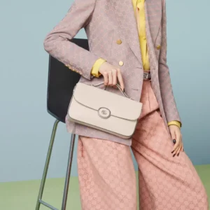 Woman wearing a stylish blazer and yellow shirt, holding a Gucci Petite GG Series Small Shoulder Bag, showcasing modern design and double-G logo against a pastel background.