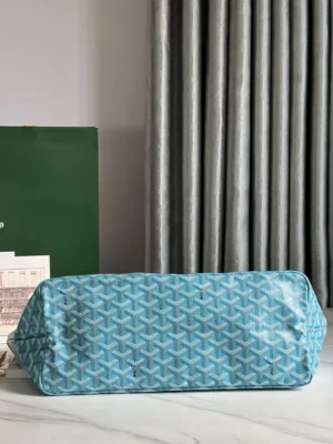 Goyard Belvedere II Tote in blue leather, featuring a distinctive geometric pattern, displayed on a marble surface with a green backdrop and draped curtains.