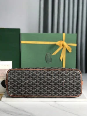 Goyard Citadin Mailman Bag displayed on a marble surface, featuring a distinctive woven pattern and leather accents, with a green gift box and yellow ribbon in the background, highlighting its elegant design and functionality.