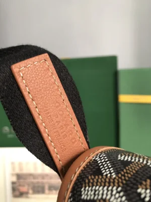 Close-up of Goyard Citadin Mailman Bag handle featuring a leather tag, showcasing the bag's distinctive pattern and craftsmanship, with green boxes in the background.