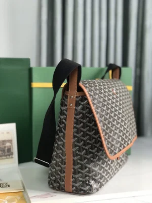 Goyard Citadin Mailman Bag in grey and brown, featuring a shoulder strap, displayed beside green boxes, emphasizing its stylish and functional design.