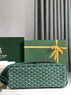 Goyard Citadin Mailman Bag in green, featuring signature patterned design, placed on a marble surface with a branded gift box and ribbon in the background, highlighting luxury and functionality.