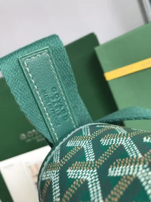 Goyard Citadin Mailman Bag detail showcasing green patterned fabric and logo tag, emphasizing luxury craftsmanship and design features.