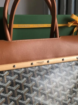 Goyard Saigon Tote bag featuring a brown leather handle, signature Goyard pattern, and branded hardware, displayed with a green gift box and ribbon.