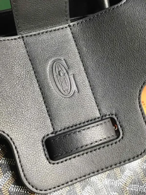 Close-up of Goyard Saigon Tote bag's textured black leather handle featuring embossed logo, highlighting luxury craftsmanship and design details.