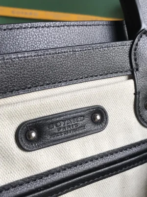 Goyard Saigon Tote bag close-up showcasing the logo tag, featuring a blend of black leather and cream canvas, emphasizing luxury craftsmanship and design details.
