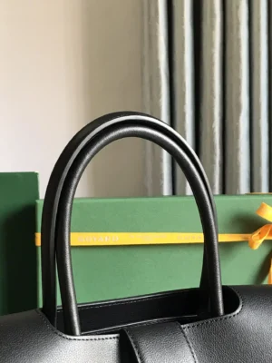 Goyard Saigon Tote bag featuring elegant black leather handles, with green Goyard packaging and decorative yellow ribbon in the background.