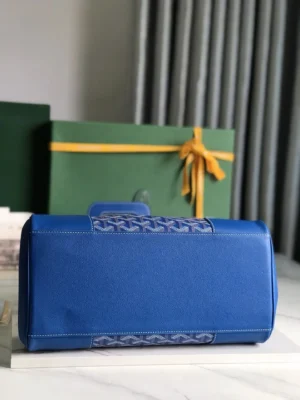 Goyard Saigon Tote bag in blue leather with distinctive design elements, displayed against green boxes with yellow ribbons, emphasizing luxury and elegance.