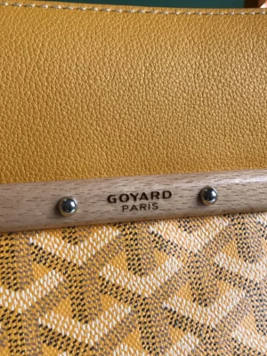 Goyard Saigon Tote bag detail featuring yellow leather and wood accents with Goyard Paris branding, emphasizing luxury and elegance.