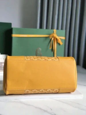 Goyard Saigon Tote bag in yellow leather with iconic logo detail, displayed on a marble surface next to a green gift box, highlighting luxury and elegance.
