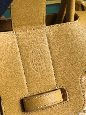 Goyard Saigon Tote bag detail featuring embossed 'G' logo on textured yellow leather, highlighting luxury craftsmanship and design.