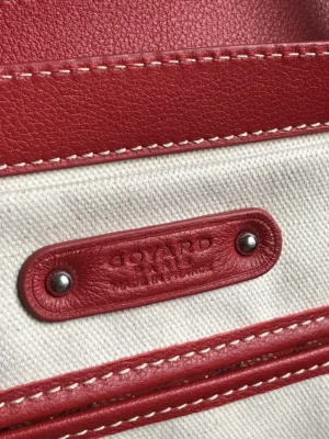 Goyard Saigon Tote bag close-up showcasing the brand logo, red leather accents, and canvas material, emphasizing luxury and craftsmanship.
