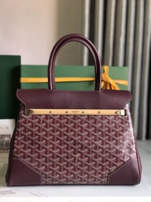Goyard Saigon Tote bag in burgundy with gold accents, showcasing its elegant design and distinctive pattern, placed beside a green box, emphasizing luxury and style.