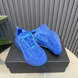 AMIRI Trainer sneakers in vibrant blue color, displayed on a black shoe box with a textured background, emphasizing luxury footwear style.
