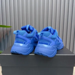 Blue AMIRI Trainer sneakers displayed from the back, showcasing mesh and rubber materials, set against a minimalist background.