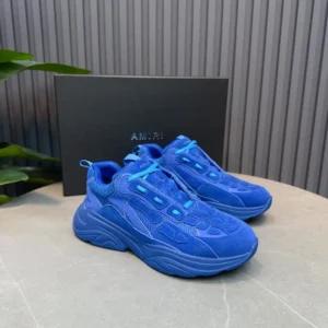 AMIRI Trainer sneakers in vibrant blue, displayed on a stone surface with a branded box in the background, highlighting luxury footwear design.