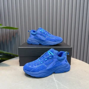 AMIRI Trainer sneakers in vibrant blue suede, displayed on a black box with a textured background, showcasing luxury footwear design.