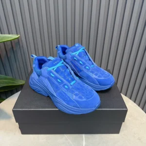 Blue AMIRI Trainer sneakers displayed on a black box against a textured background, highlighting luxury footwear design.