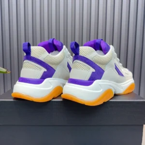 AMIRI Trainer replica sneaker featuring a white base with purple and orange accents, displayed from the rear on a dark surface, highlighting its chunky design and modern style.